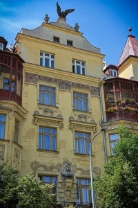 The five-story building at No. 1552 features a bust of George of Poděbrady on its facade and a falcon statue on the mansard gable.